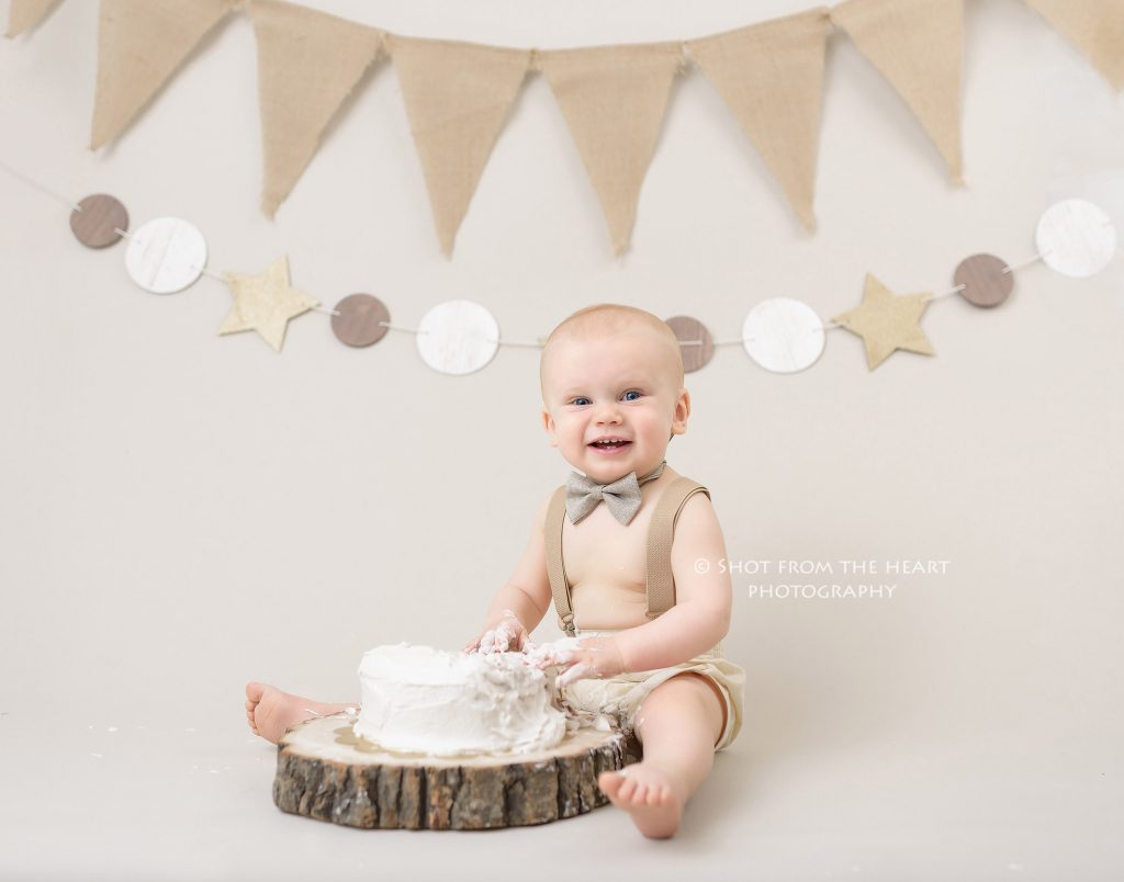 baby boy smashing first birthday cake photography with tan neutral rustic backdrop theme