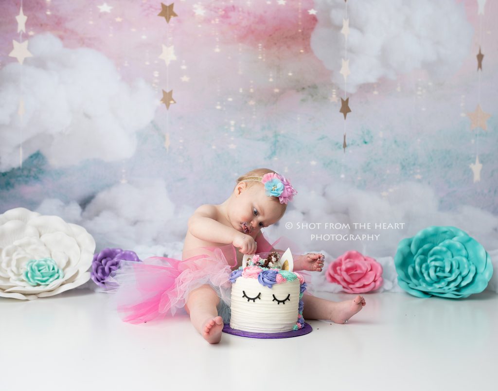 Unicorn birthday cake smash photography session with pink, purple, teal, and white colors. 