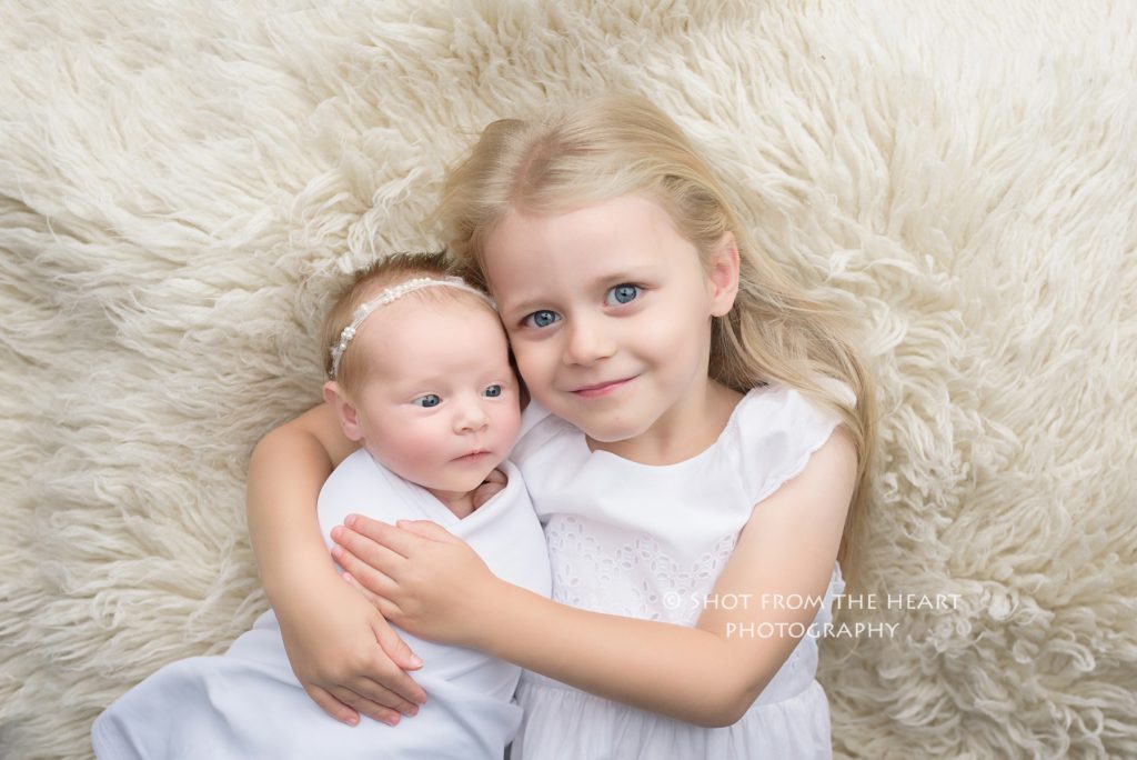 big sister in white dress holding newborn baby child photography