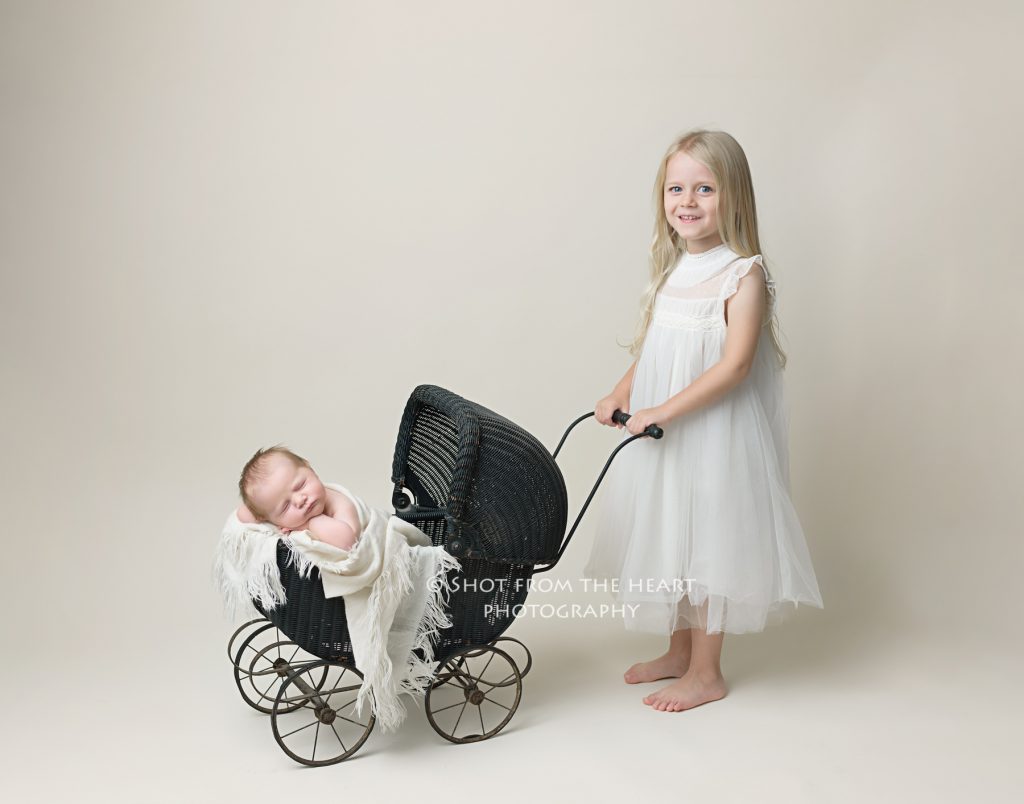 big sister in white dress pushing newborn baby in vintage antique pram stroller