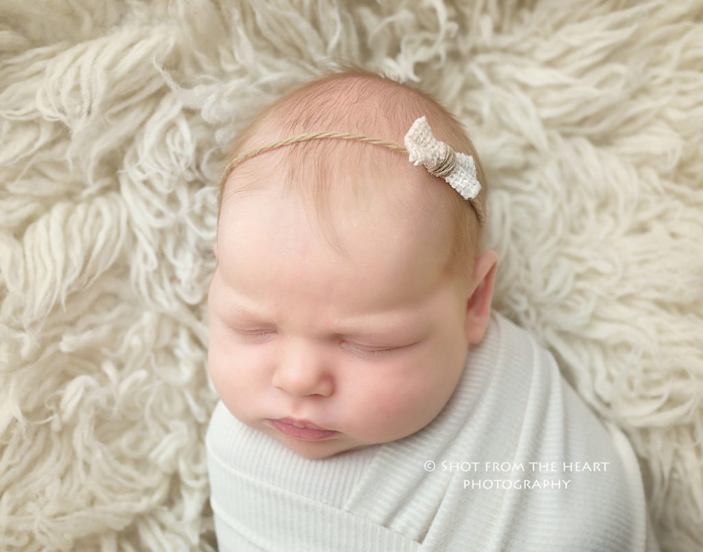 newborn baby girl with headband bow on white fluffy background Alpharetta photographer