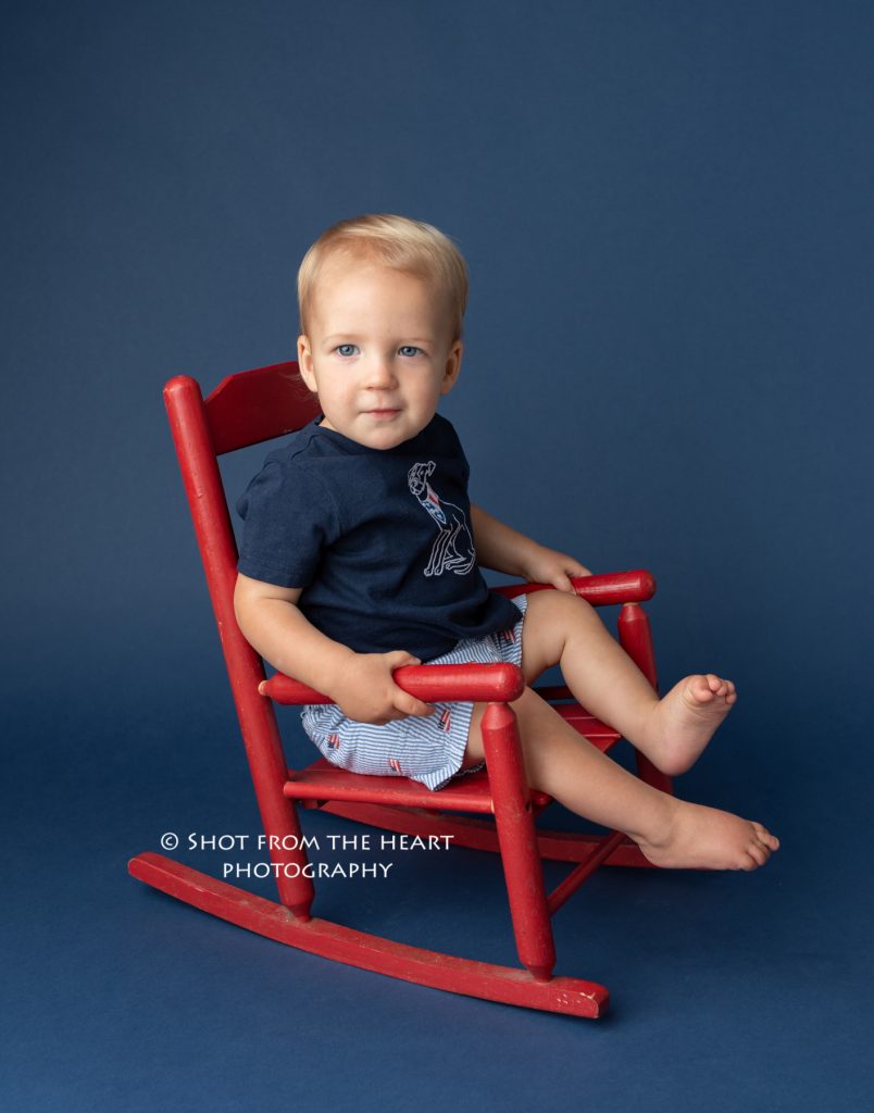 first birthday portraits. little boy in red rocking chair on navy backdrop. 