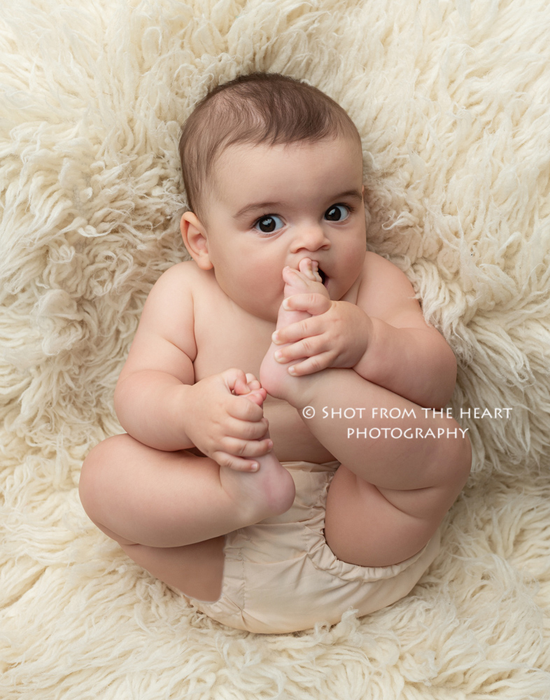 expressive baby photography on float cream rug chewing on toes