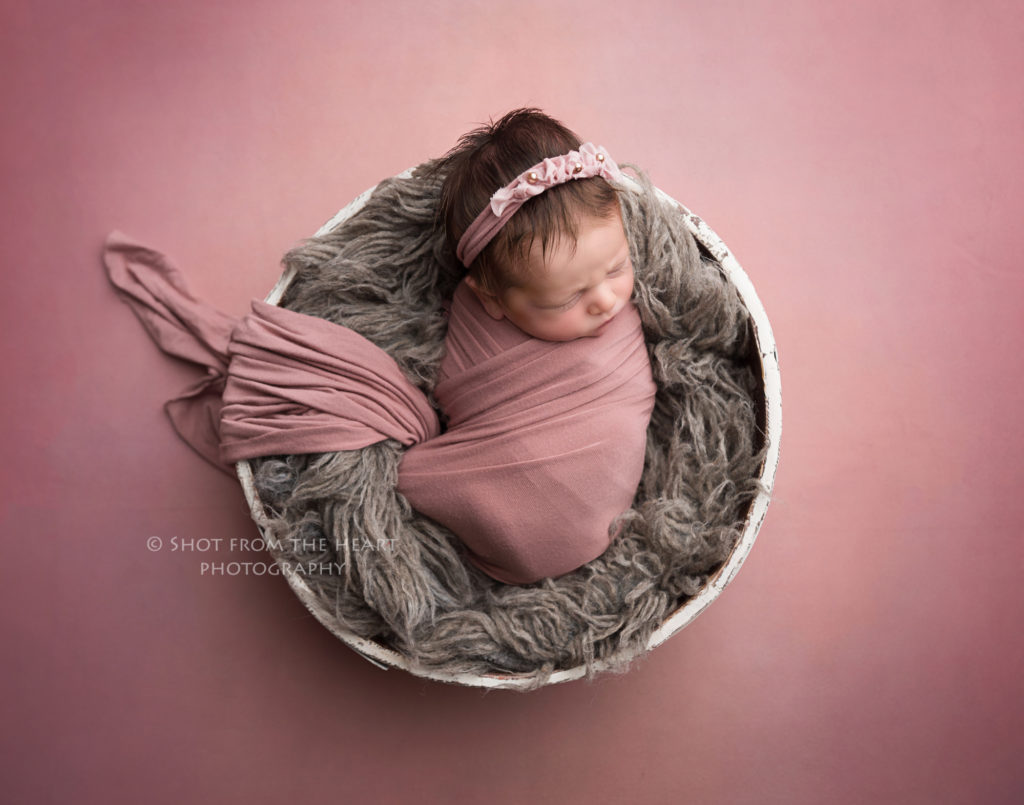 newborn baby photography with baby in pink swaddle grey and pink background