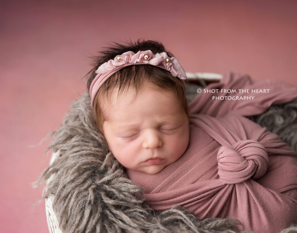 newborn baby girl in swaddle with pink backdrop